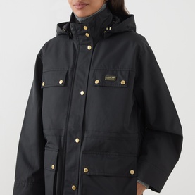 Model wearing Barbour International Molina Showerproof Coat in black with gold snap buttons, detachable hood, and chest flap pockets.