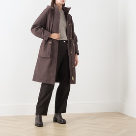 Model wearing Barbour International truffle hooded coat with patch pockets, styled with grey knit, black trousers and ankle boots