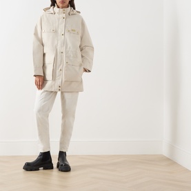 Model wearing Barbour International Molina Showerproof Short Jacket in Moonbeam with detachable hood, styled with white trousers and black chunky