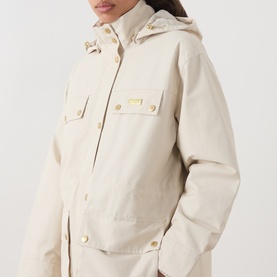 Model wearing Barbour International Molina Showerproof Short Jacket in Moonbeam with detachable hood, chest flap pockets and gold-tone snap buttons.