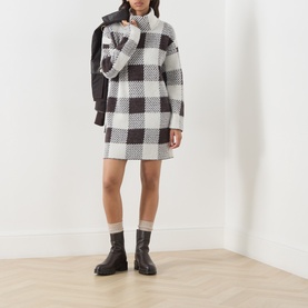 Model wearing Barbour International multi check knit dress with dark ankle boots, styled with an oversized dark jacket draped over shoulder.
