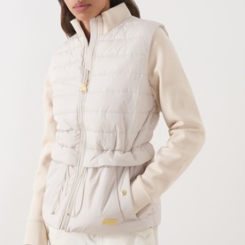 Model wearing Barbour International Ari Hybrid Quilted Jacket in Moonbeam with sweatshirt sleeves, stand collar, drawcord waist and gold-toned
