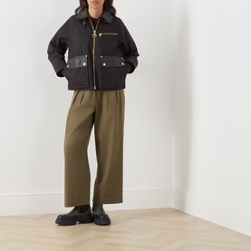 Model wearing Barbour International dark brown cotton jacket with gold zip and pocket details, styled with khaki wide-leg trousers and black loafers