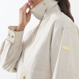 Model wearing Barbour International Moonbeam jacket, close-up showing gold button cuffs, zip collar, and branded gold logo badge