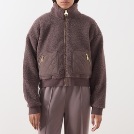 Model wearing Barbour International truffle fleece bomber jacket with gold zip, quilted pockets, and matching trousers.