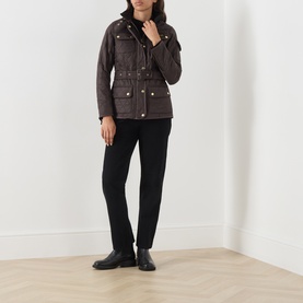 Model wearing Barbour International truffle quilted jacket with gold-tone press studs, styled with black trousers and ankle boots.
