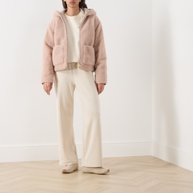 Model wearing Barbour International Ramona Zip-Up Fleece Jacket in Nutmeg, sherpa fleece with hood and patch pockets, styled with cream wide-leg