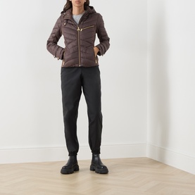 Model wearing Barbour International truffle quilted hooded jacket with gold zip detail, styled with black joggers and chunky boots