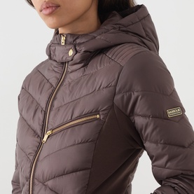 Model wearing Barbour International truffle quilted hooded jacket with gold-tone zip detail and side panel contrast.