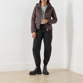 Model wearing Barbour International truffle quilted hooded jacket with black joggers and chunky black ankle boots
