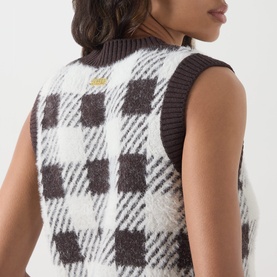 Model wearing Barbour International multi check knitted vest, back view, styled over dark long-sleeve top. Gold logo badge visible.