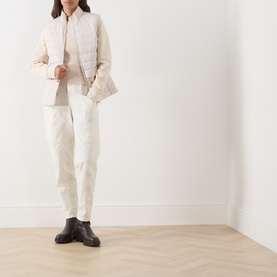 Model wearing Barbour International Cyrus Dropped-Shoulder Sweater in Nutmeg, styled with cream quilted gilet, white trousers and dark ankle boots.