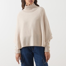 Model wearing Barbour International moonbeam knit poncho with turtleneck, button cuff detail, styled with blue jeans.