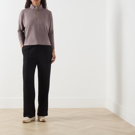 Model wearing Barbour International Kemora Logo Half-Zip Sweatshirt in Truffle with black wide-leg trousers and cream trainers.