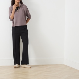 Model wearing Barbour International Kemora Logo Half-Zip Sweatshirt in Truffle with black wide-leg trousers and cream flat shoes.