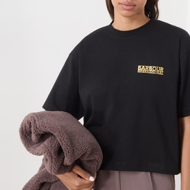 Model wearing Barbour International black cotton T-shirt with yellow logo print, styled with a dark brown fleece jacket over arm.