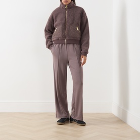 Model wearing Barbour International Truffle trousers, styled with a matching brown zip-up fleece jacket and black shoes.