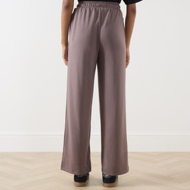Model wearing Barbour International Truffle wide-leg trousers, elasticated waist, rear view, styled with black top and wooden heeled shoes.