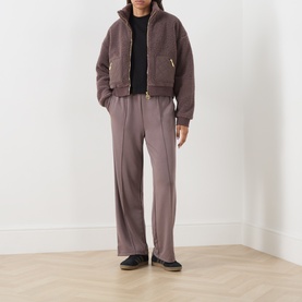 Model wearing Barbour International Truffle trousers, styled with a matching cropped zip jacket and black trainers.