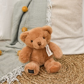 Dou Dou brown plush teddy bear with soft fluffy fur, seated on a woven mat with cushions in background