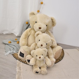 Dou Dou cream plush teddy bears in three sizes, arranged together on a woven tray with gold bead decorations nearby.