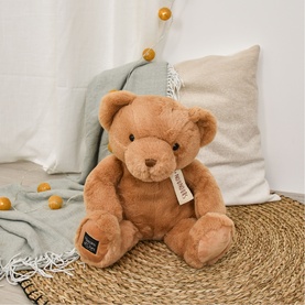 Dou Dou brown plush teddy bear, seated upright with jointed limbs and label tag, styled with cushions and wicker tray