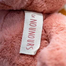 Dou Dou pink plush teddy bear close-up showing Le Nounours label stitched into soft pink fluffy fur