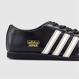 Adidas Japan trainers in core black with cream white three stripes, gold branding detail, black rubber sole, leather upper.