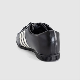 Adidas black leather trainer with cream white three-stripe detail, rear view, black rubber sole.