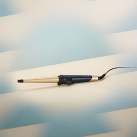 Tapered hair curling wand with cream-coloured barrel and dark navy handle, shown on a soft blue geometric background