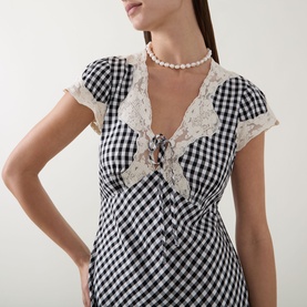 Model wearing Rixo Beth Check Black dress with lace collar detail and tie-front neckline, styled with a pearl choker necklace.