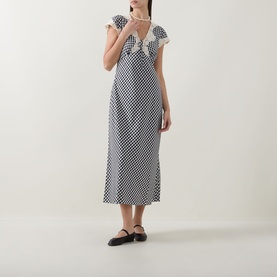 Model wearing Rixo Beth Check Black dress in monochrome check print, midi length, flutter sleeves with lace trim, styled with black Mary Jane flats