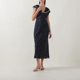 Model wearing Rixo Bethea Dot Dress in Layla Dot Navy, midi-length bias-cut silhouette with ruffle V-neckline and polka dot print, styled with nude