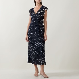Model wearing Rixo Bethea Dot Dress in Layla Dot Navy, midi-length with ruffle V-neckline, polka dot print, styled with nude heeled mules.