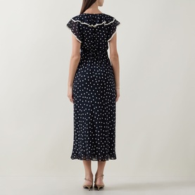 Model wearing Rixo Bethea Dot Dress in Layla Dot Navy, midi length with ruffle detail and polka dot print, back view.