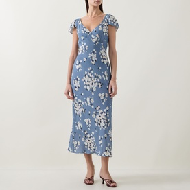 Model wearing Rixo Cathy Floral Dress in Amelia Bouquet Blue; V-neckline, short sleeves, bias-cut midi length, styled with brown heeled sandals.