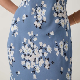 Model wearing Rixo Cathy Floral Dress in Amelia Bouquet Blue, bias-cut midi with white floral print and empire waist detail visible.