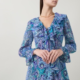 Model wearing Rixo Bianca Abstract Blue silk dress with V-neck ruffle detail and flared sleeves, styled with a gold chain necklace.