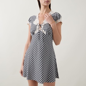 Model wearing Rixo Lacie Check Dress in black gingham with lace trim V-neckline, tie detail, puff sleeves, and empire waist mini length.