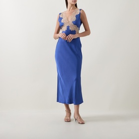 Model wearing Rixo Lysandra Lace Dress in Iris Blue, midi length with V-neckline and gold lace trim, styled with strappy heels