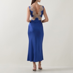 Model wearing Rixo Lysandra Lace Dress in Iris Blue satin with gold lace back detail, midi length, styled with strappy heels.