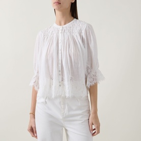 Model wearing Rixo ivory cotton blouse with lace trim hem and cuffs, smocked neckline, styled with white trousers