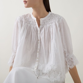 Model wearing Rixo ivory cotton blouse with lace trim detailing, smocked bodice and three-quarter sleeves, styled with white trousers