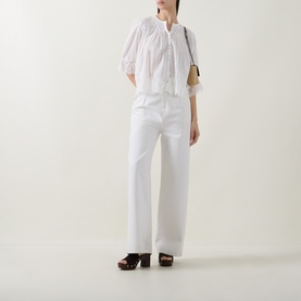 Model wearing Rixo ivory cotton top with lace trim and puff sleeves, styled with white wide-leg trousers and dark wooden heeled mules
