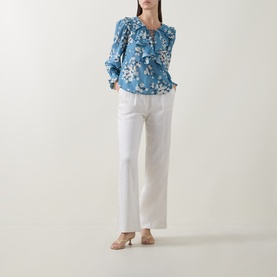 Model wearing Rixo top in Amelia Bouquet Blue floral print with ruffle detail, styled with white wide-leg trousers and nude heels