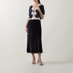 Model wearing Rixo Layla Dot Navy top with black midi skirt and black strappy heels