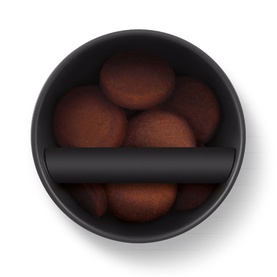 Matte black round bowl filled with chocolate brown cookies, viewed from above, with a black handle divider across the centre