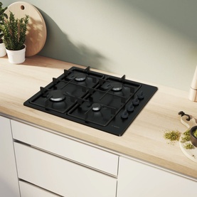Bosch Series 2 60cm Black Enamel Gas Hob built into a light wood kitchen countertop, shown with white cabinetry and plants in background.