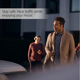 Model wearing Sony Linkbuds True Wireless Earbuds White, walking outdoors at night in a beige coat, with traffic visible behind him.