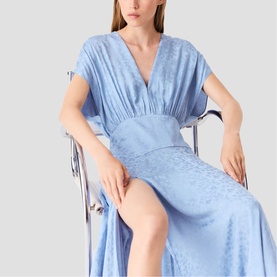 Model wearing a pale blue satin midi dress with V-neckline, short sleeves, cinched waist, and front split, seated on a chrome chair